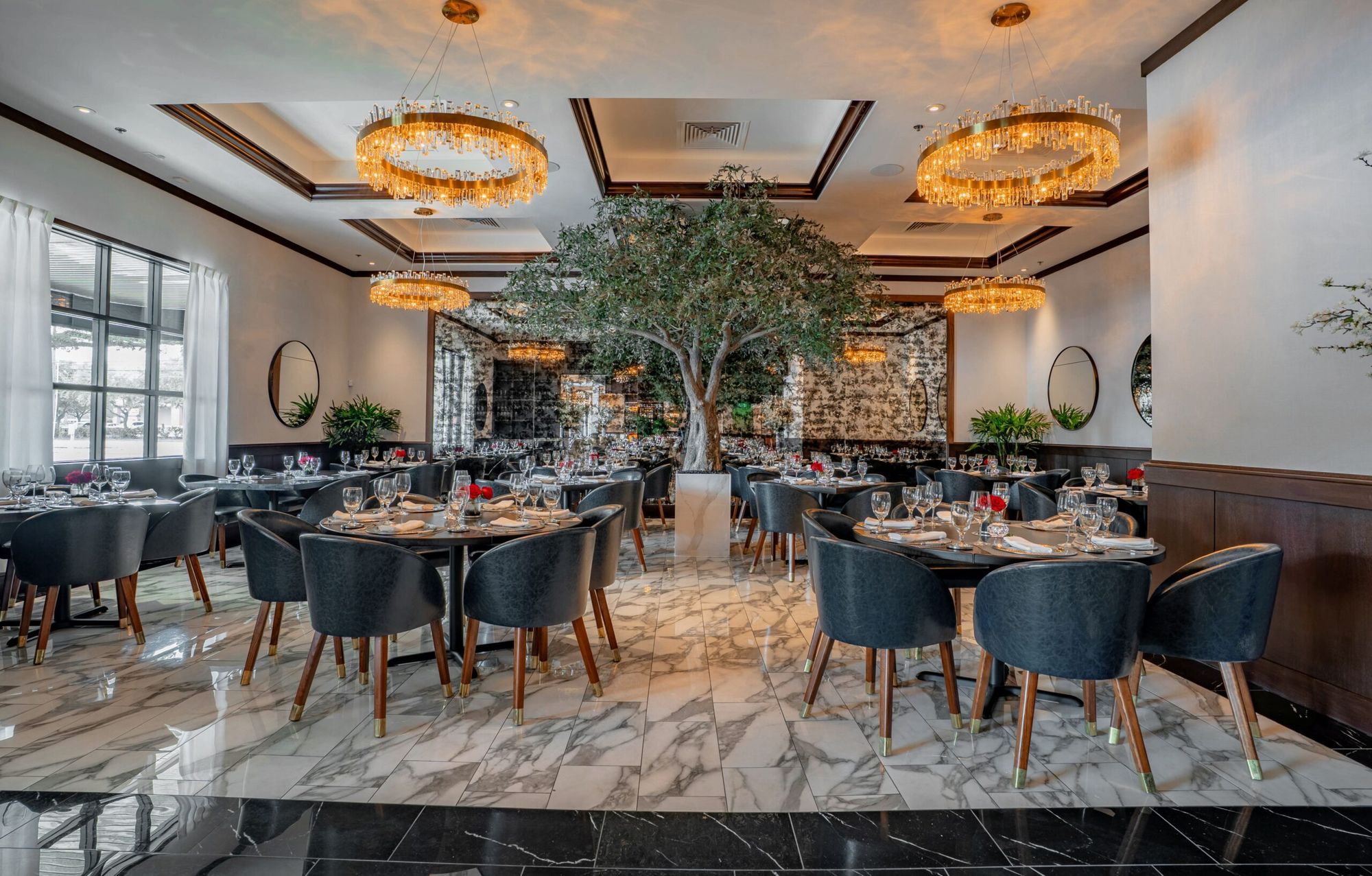 Dining room at Truluck's Houston with marble floors, an olive tree and brass chandeliers